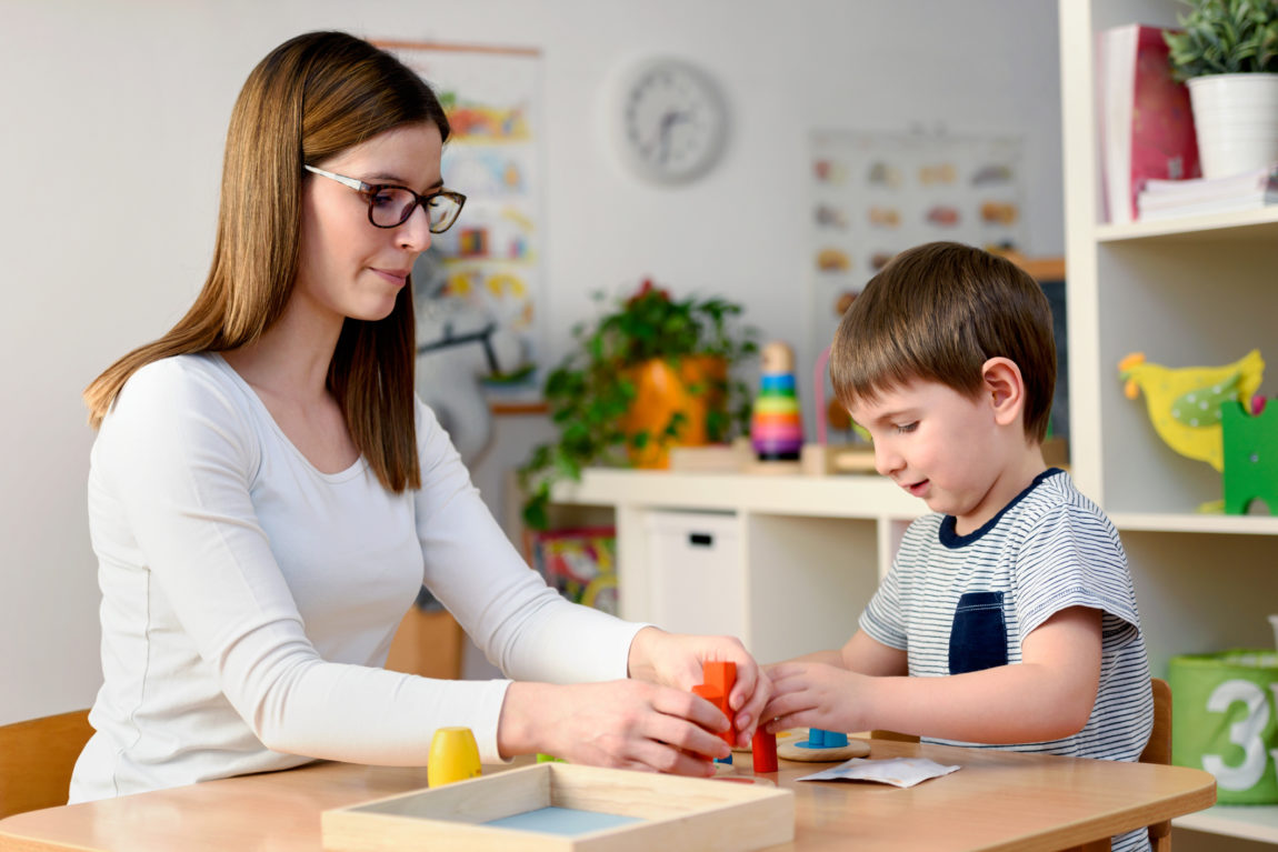 Professora apoiando aluno com deficiência intelectual em atividade adaptada na escola
