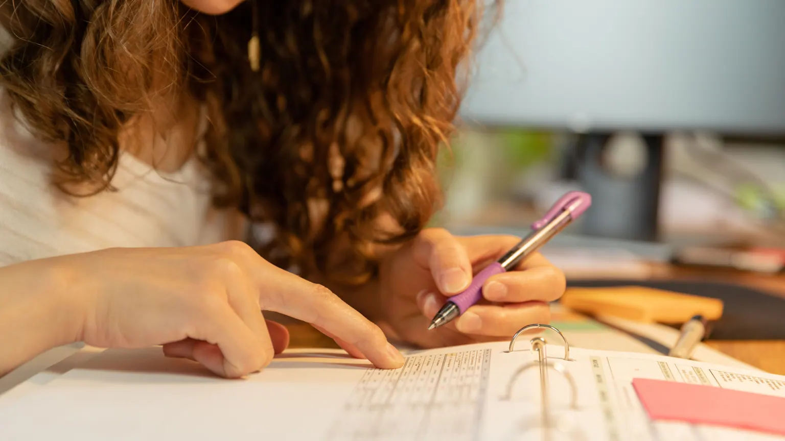 Pessoa escrevendo em um caderno ao lado de materiais escolares