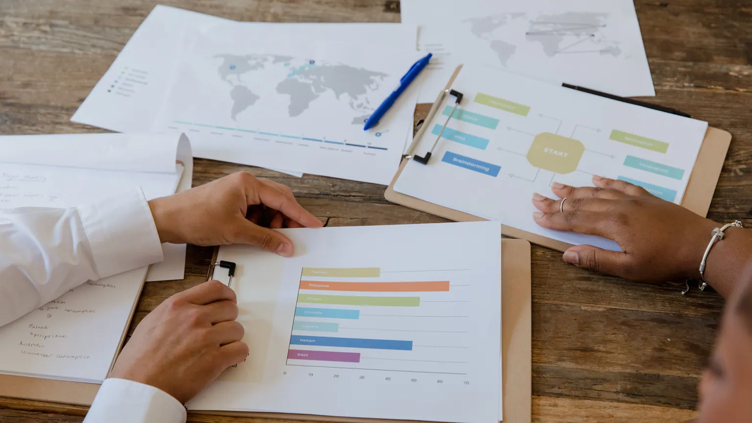 Duas pessoas analisam gráficos e documentos sobre uma mesa