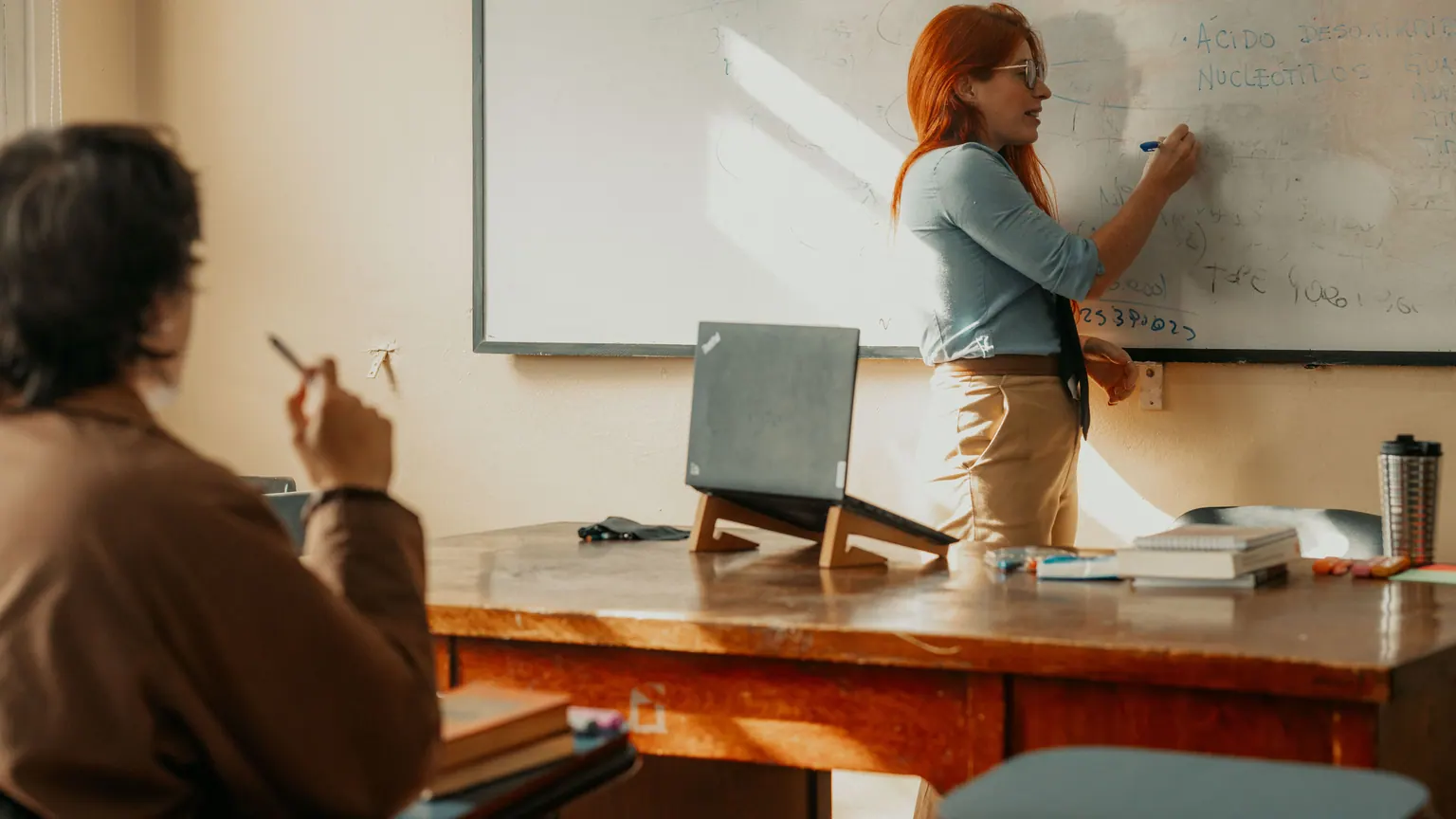 Professora escreve no quadro diante de uma turma em sala de aula