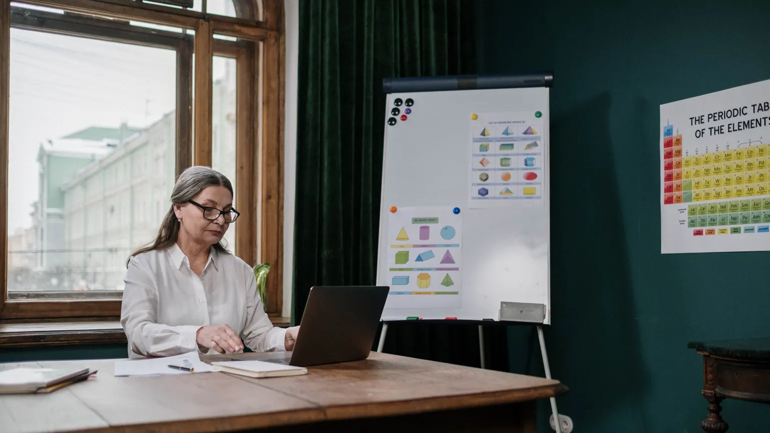 Professora organiza uma atividade ao lado de um computador em mesa de trabalho