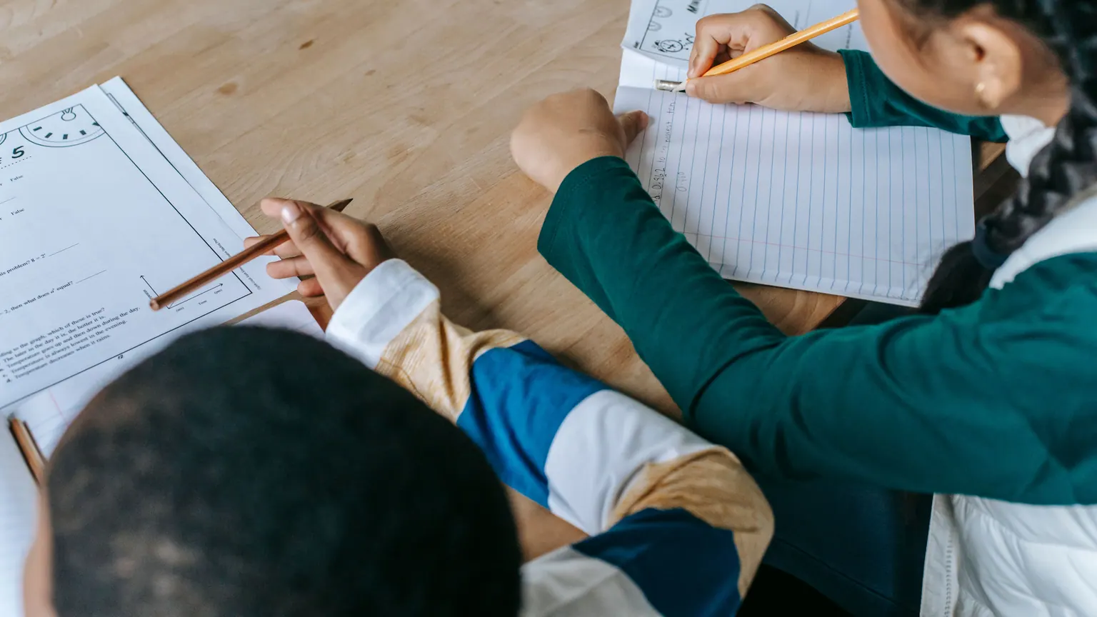 Estudantes colaboram sobre uma atividade escrita em uma mesa.