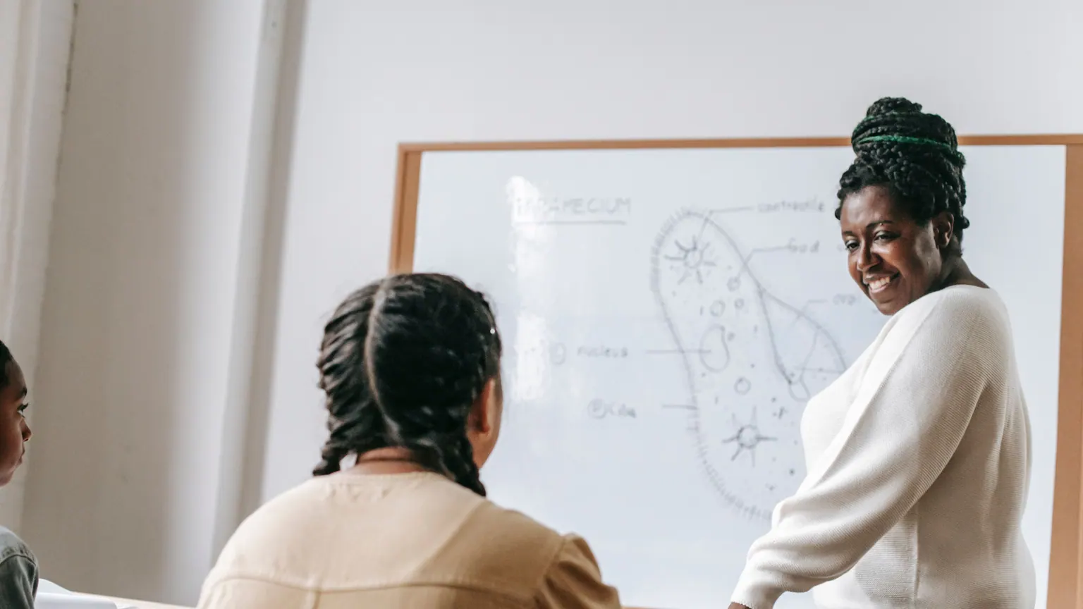 Professora conversa com uma adulta diante de um quadro em sala de aula